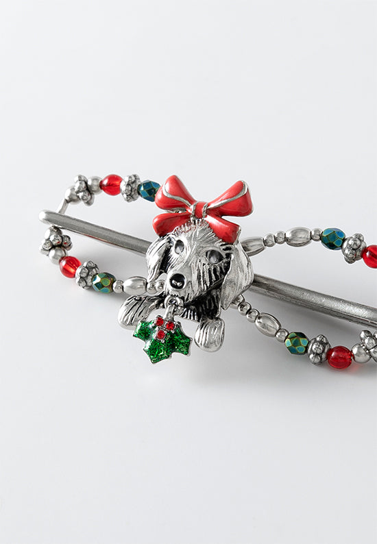 Flexi hair clip with Christmas puppy with a bright red bow holds a bundle of holly in its mouth with ruby red and iris green accents